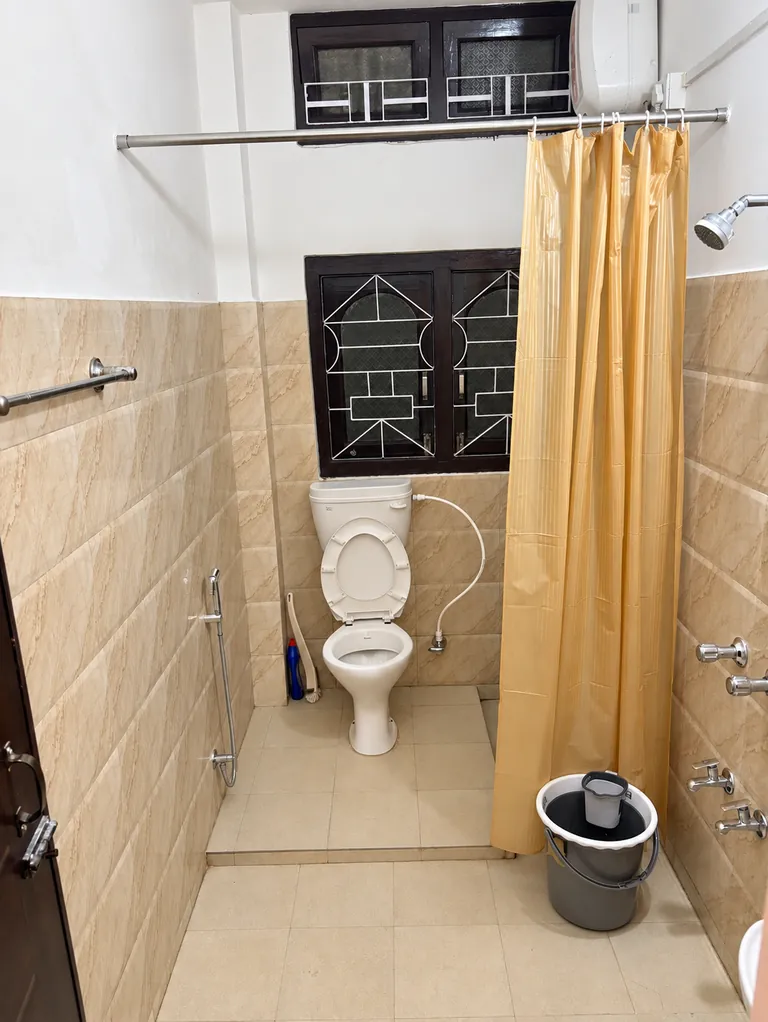Bathroom in the 1BHK with a western toilet and a curtained shower area