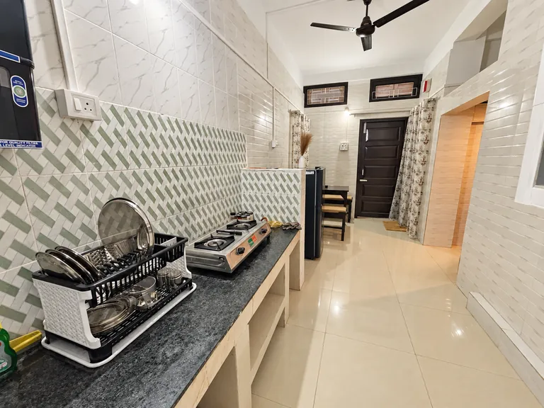 Kitchen counter with a two-burner stove and dish rack, looking down the hallway of the 1BHK