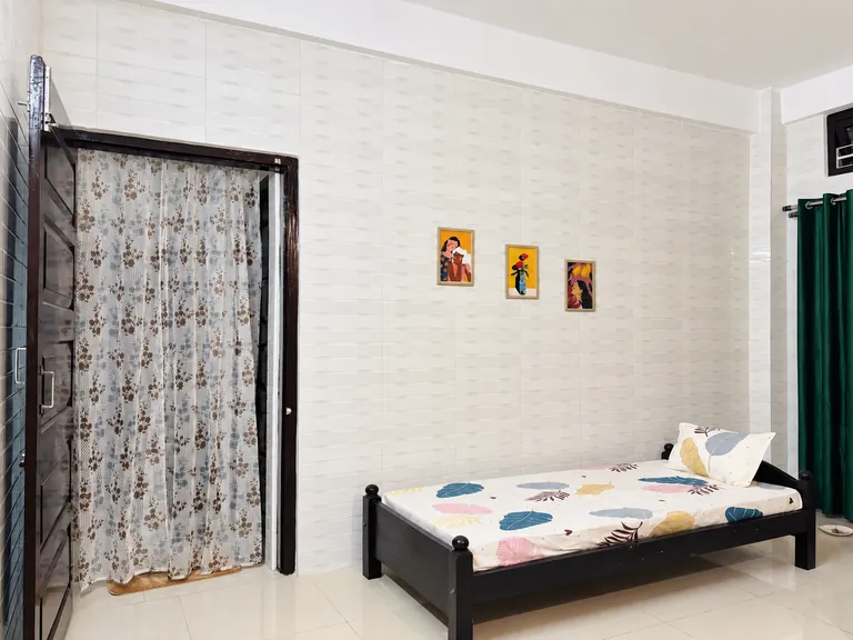 Single bed in the 1BHK living room beside a curtained doorway