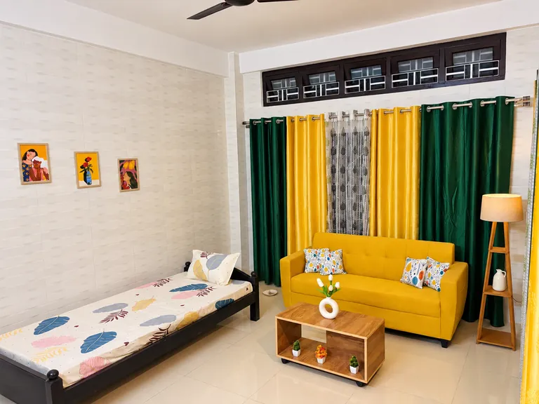 The living room of the Aurum Dwell 1BHK, with its yellow sofa and green and yellow curtains