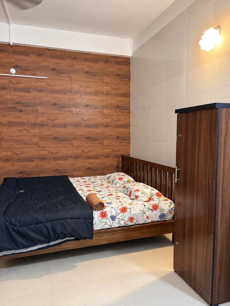 Bed against a wood-panelled wall beside a wardrobe in the 1RK