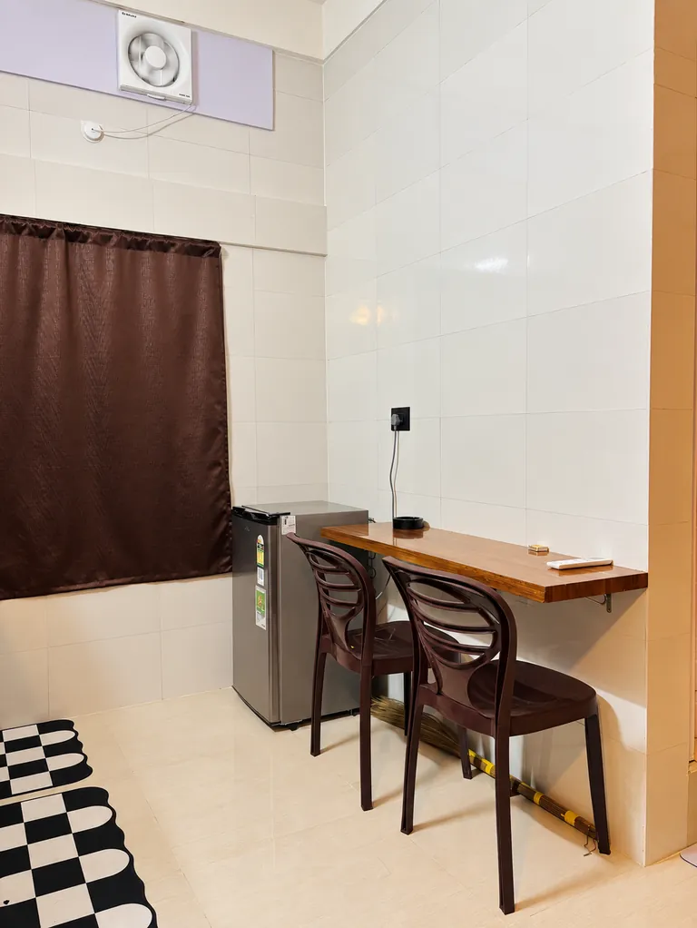 Wall-mounted breakfast counter with two chairs and a mini fridge in the 1RK