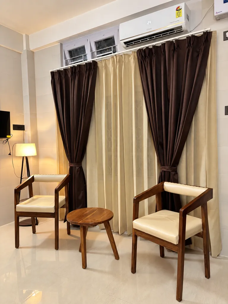 Two wooden armchairs and a round side table by the curtained windows of the 1RK